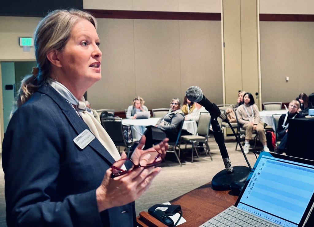 Dr. Sodergren, a white woman in a blue suit, presents from a podium in a room full of educators at the National Association for the Gifted Child Annual Conference